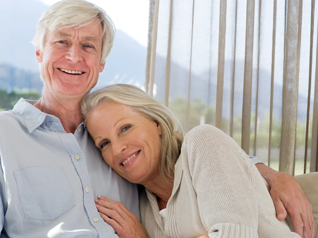 middle aged couple smiling on couch together | dental implants Cordova, TN